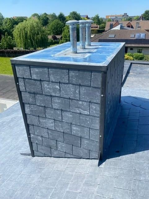 De schouw in leien van de andere zijde, met een metalen hoekprofiel op beide zichtbare hoeken en de vlak afgewerkte bovenkant waar drie schouwbuizen doorkomen