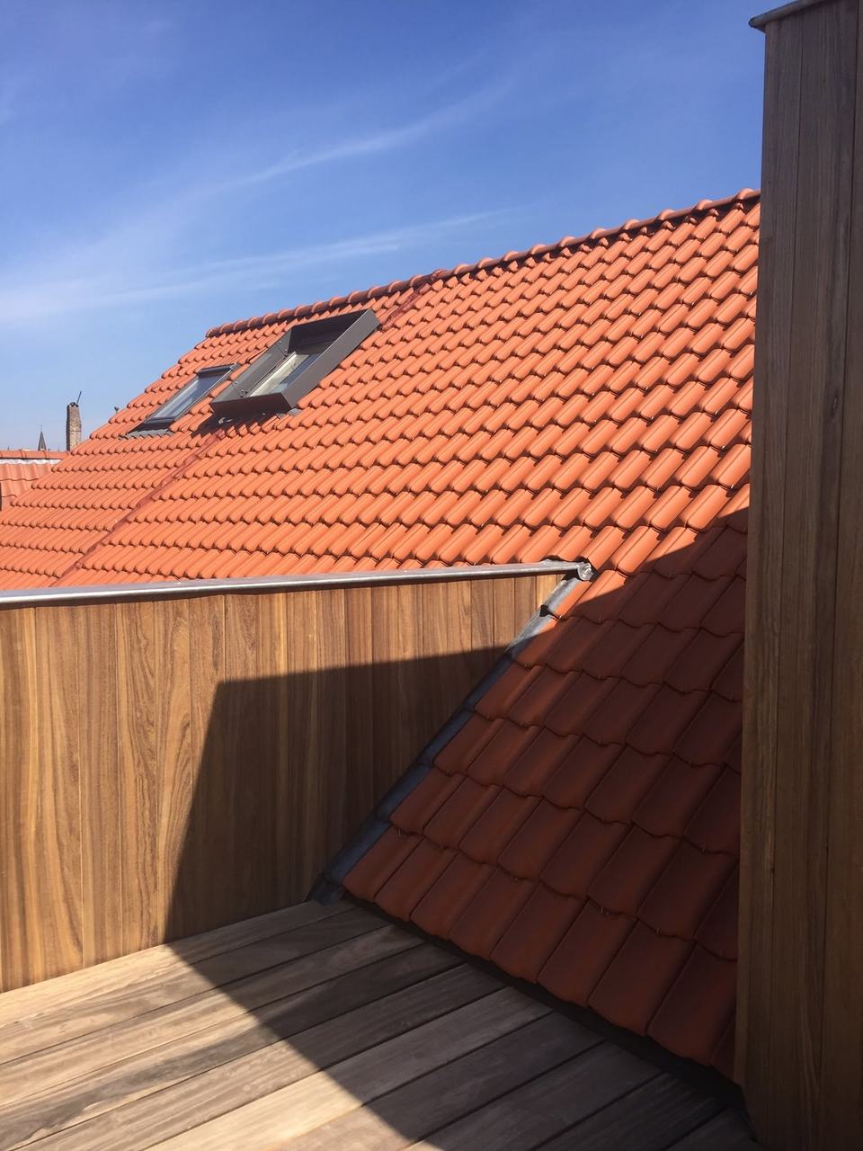 Pannendak in rode pannen met twee dakramen, gezien vanaf een houten dakterras