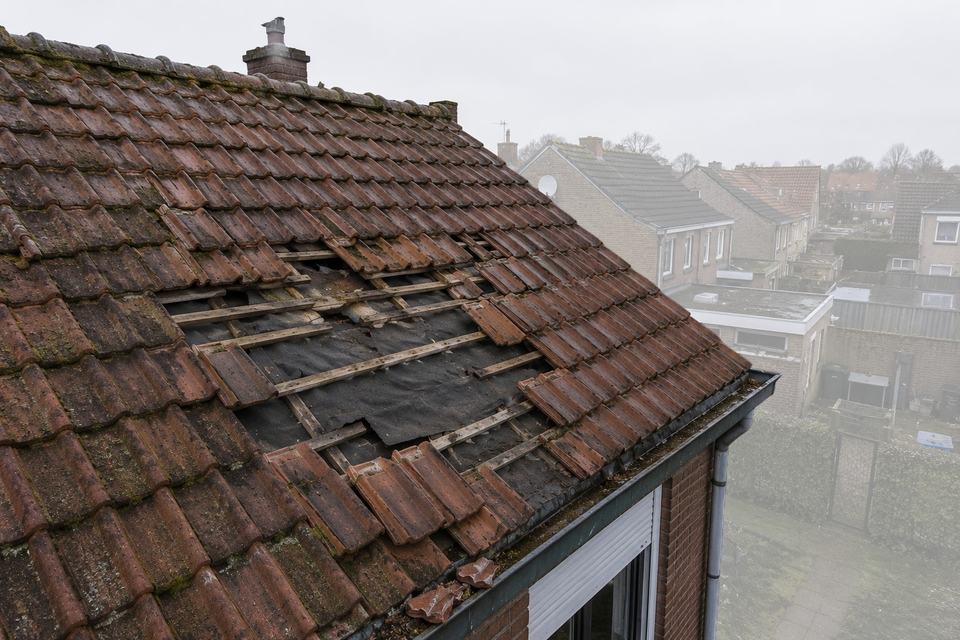 Pannendak waar een deel van de pannen is weggewaaid, met de panlatten en het gescheurde onderdak in het zicht