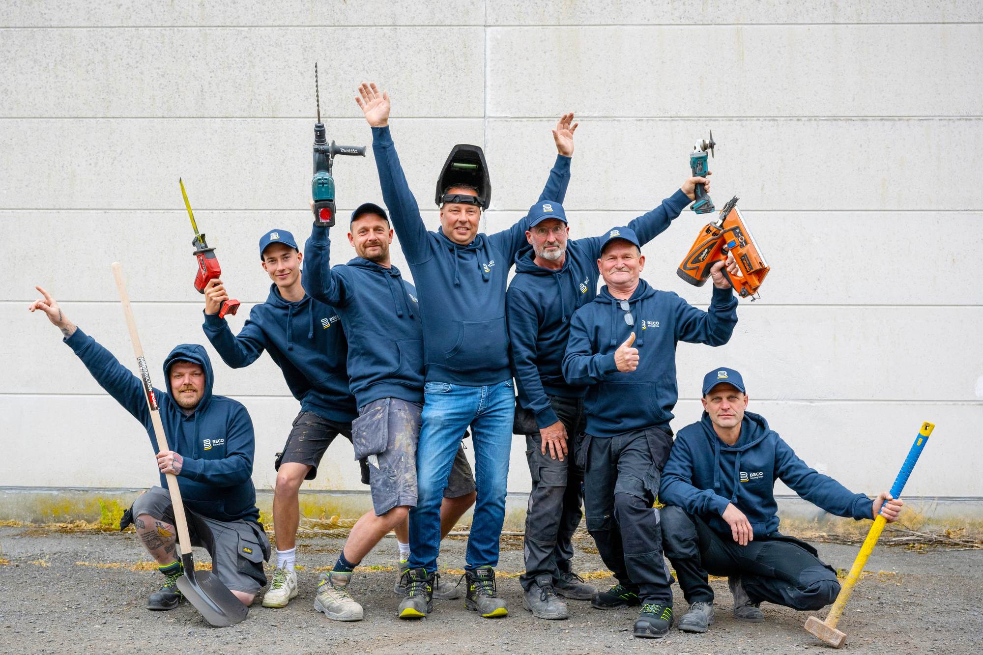 De ploeg van Beco Bouwgroep voor een betonnen wand, elk met het gereedschap van zijn eigen stiel in de hand