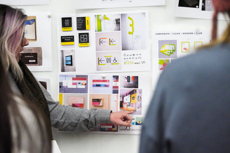 An Experiential Graphic Designer pointing to multiple sign design solutions on a whiteboard