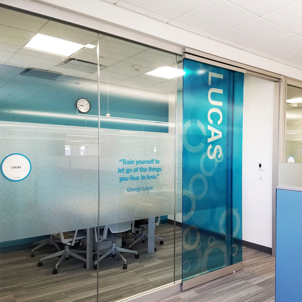 Branded window films feature a privacy band with a frosted geometric pattern and an inspirational quote; the door features a full-height random circle pattern in blue.