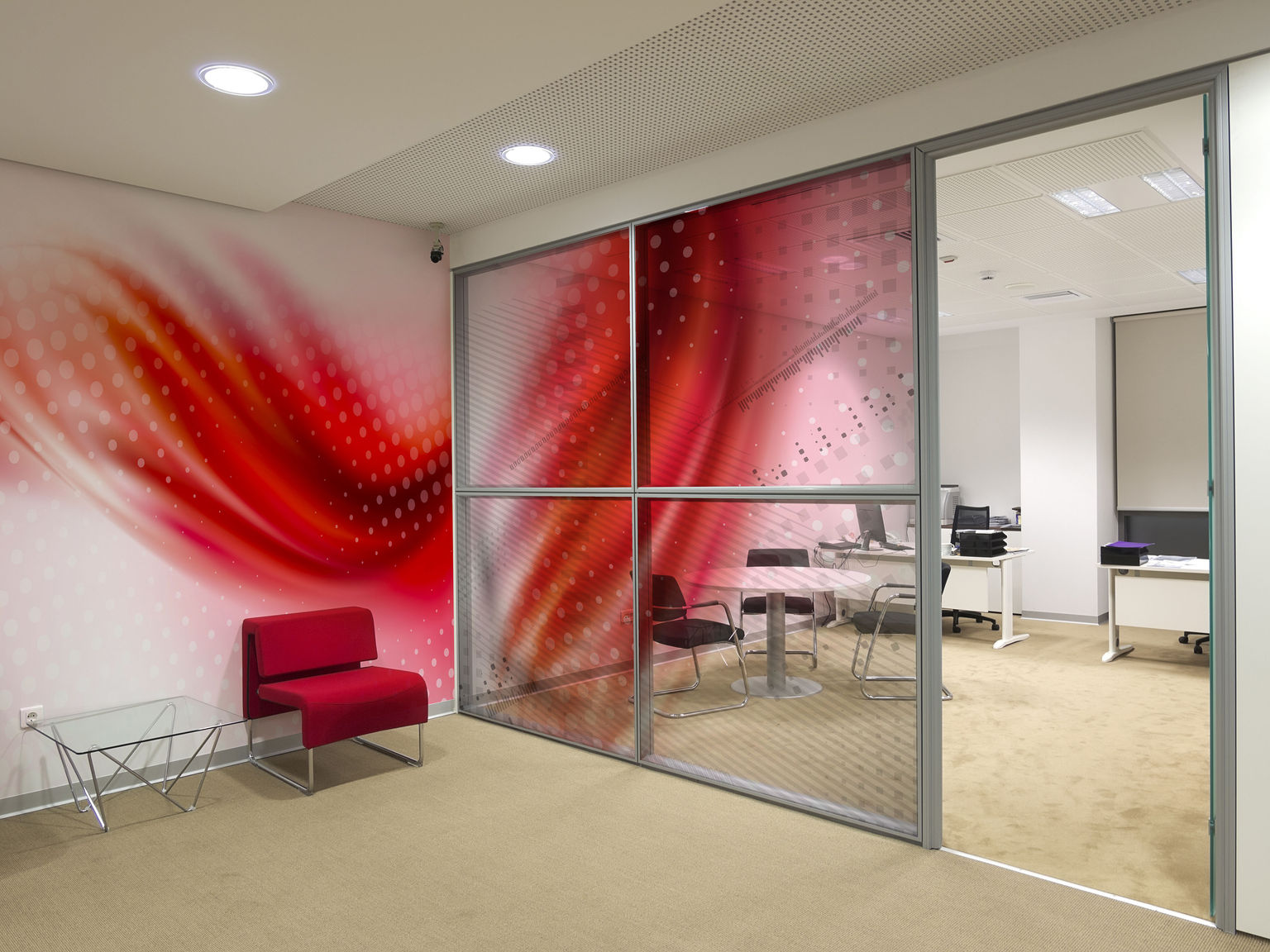 Integrated window film and wall covering graphics transition from wall to glass and feature geometric circle patterns and bold red swashes.