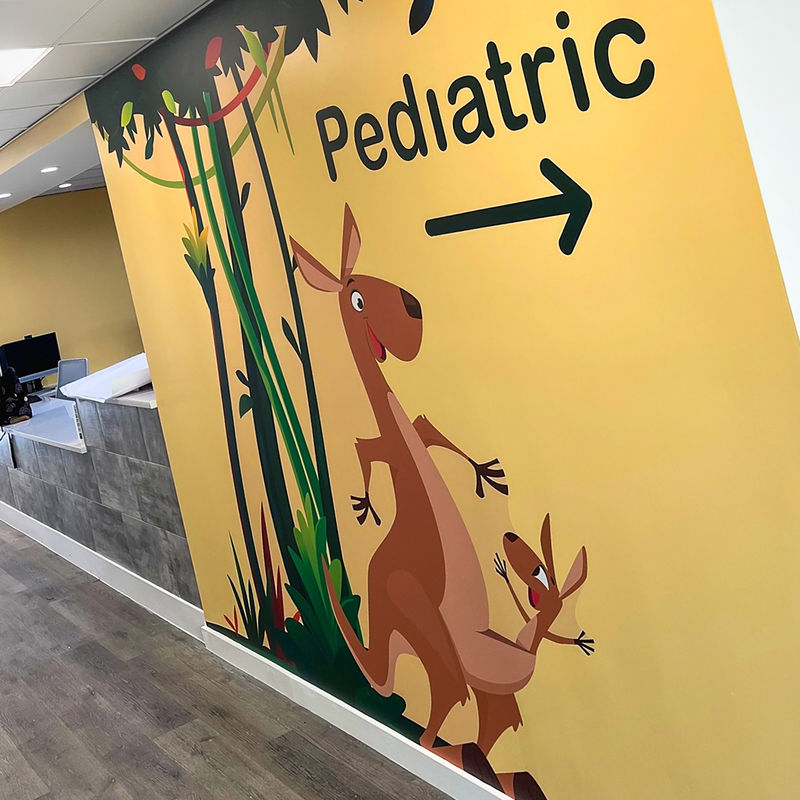 Custom wallcovering with playful kangaroo graphics on a yellow background is a wayfinding landmark in a pediatric hospital.