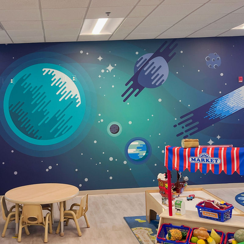 Highly cleanable custom wallcovering with child-focused graphics of stars and planets in a high-traffic kindergarten classroom.