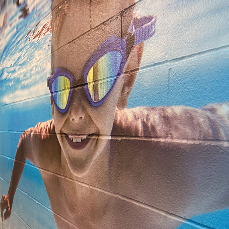 Self-adhesive custom wallcovering installed a deeply-textured block wall features an image of a young boy swimming underwater.