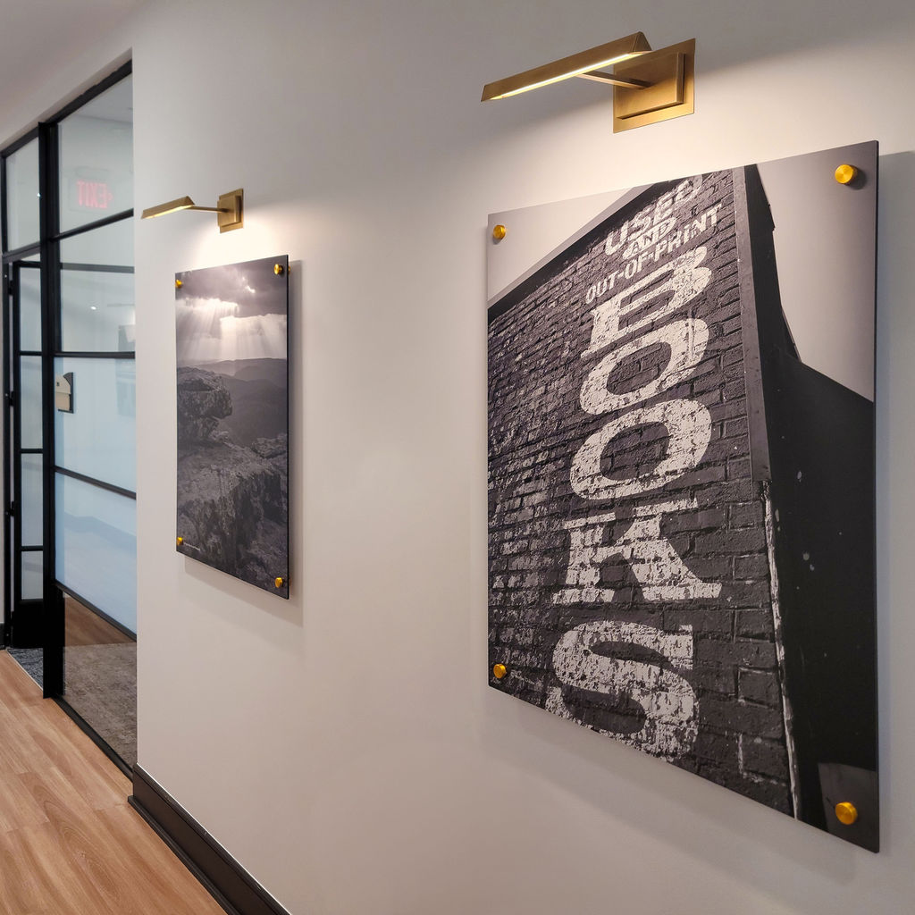 Black and white photographic art installations of local landmarks on graphic panels installed with brass accent buttons and gallery lighting in a contemporary retail bank office.