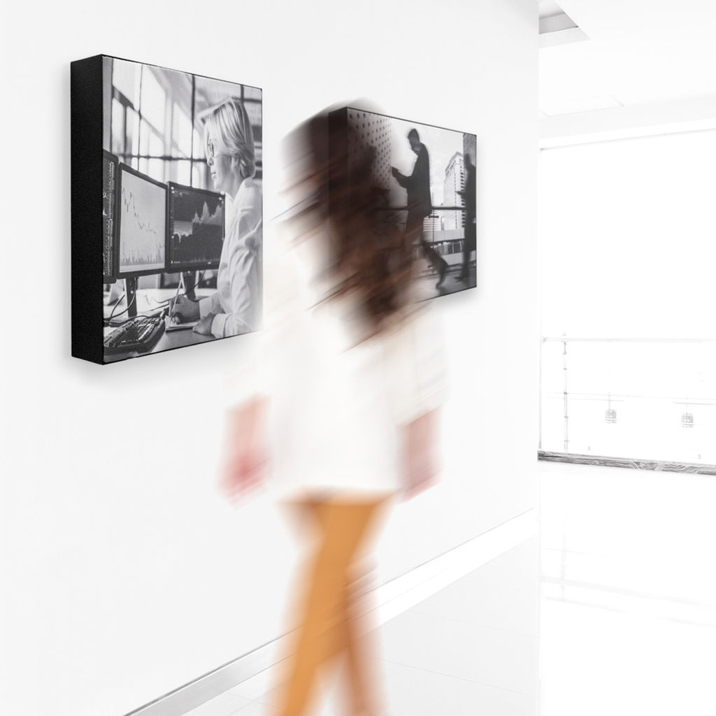 A woman walking past silicone edge graphic art installations featuring business imagery in a clean white office space.