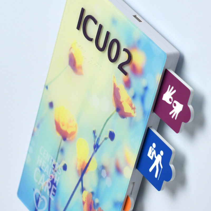 A close-up perspective of the tamper-resistant tabs on a branded ADA-compliant nurse-alert sign with a custom flower design image