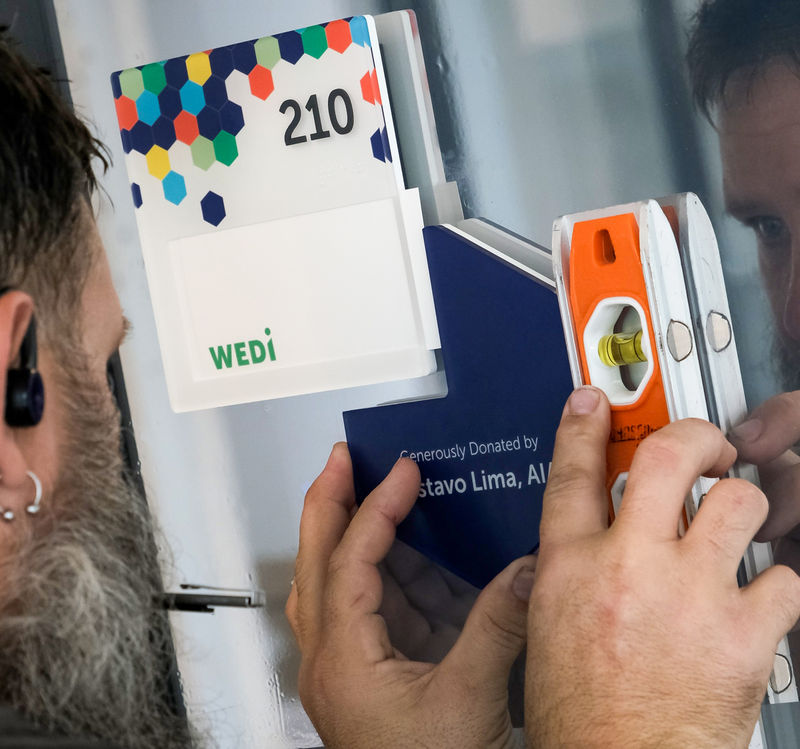 A sign installer carefully placing a room ID sign into place with a level.