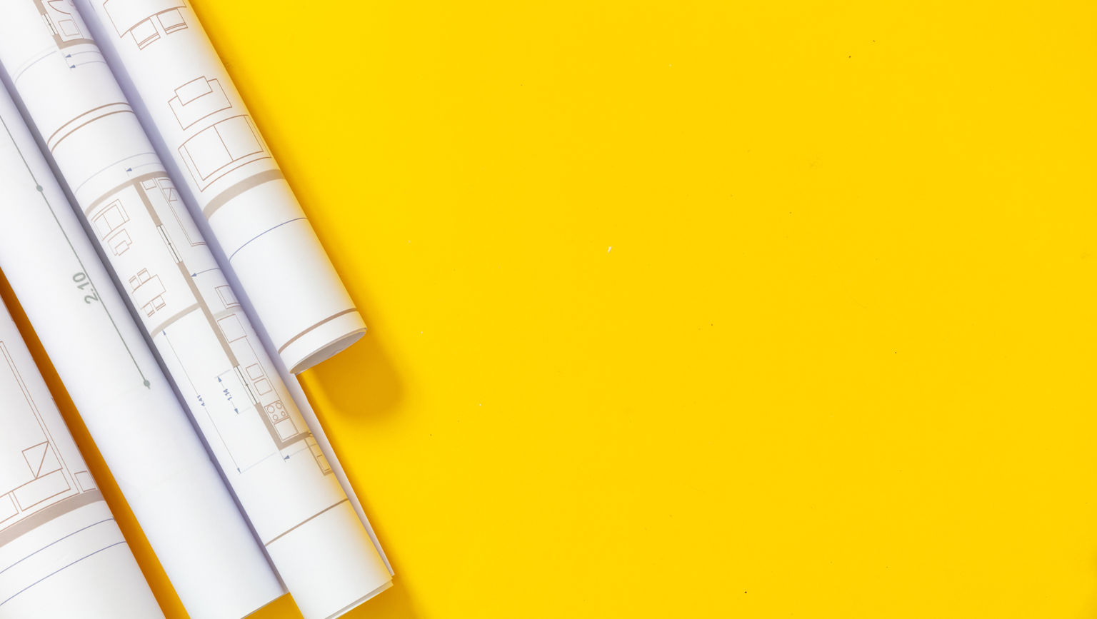Three large site surveys rolled up on white paper on a yellow background.