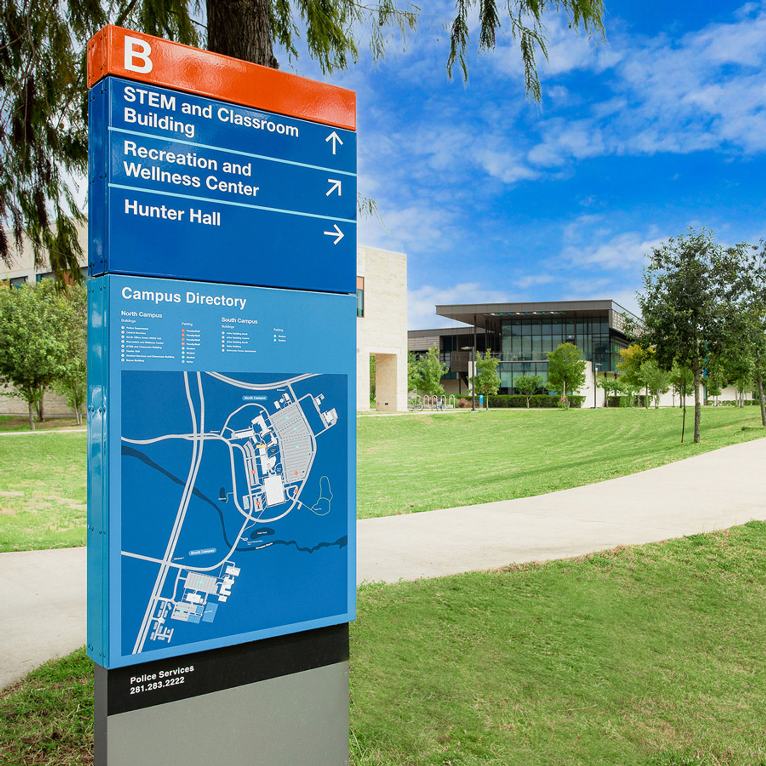 Pedestrian wayfinding directory sign with campus map with two University of Houston academic buildings in the background.