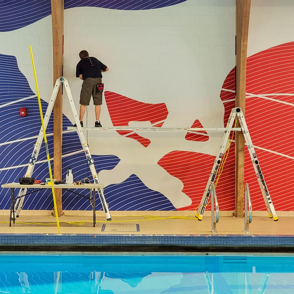 An installer on scaffolding applying large scale Amplify wallcovering on a High School pool wall.