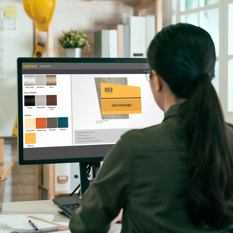 An interior designer in her office works on Takeform's online "Design Center" to create a room identification sign concept featuring concrete and yellow finishes to complement her project.
