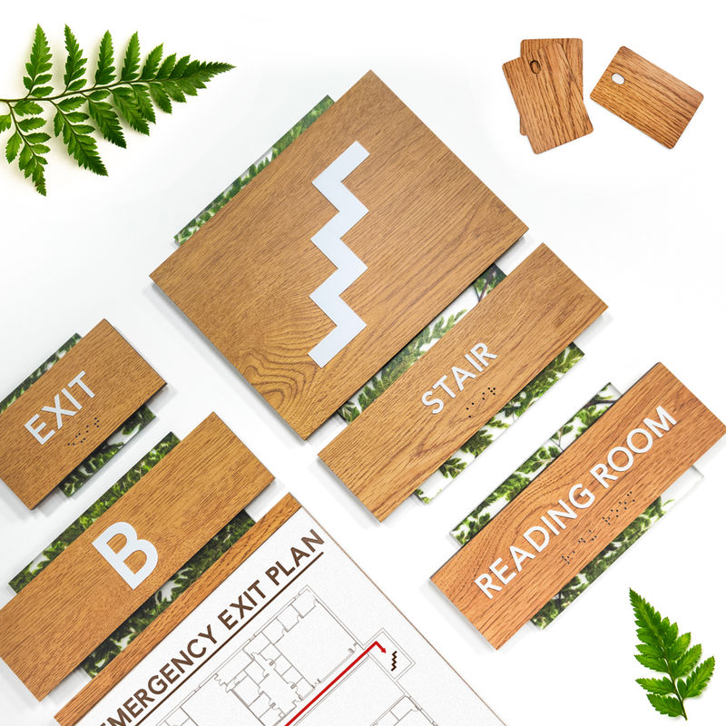 "Exit," "Stair," "Reading Room," and evacuation signs from biophilic sign system design featuring woodgrain laminate and a fern-themed encapsulated acrylic finish.