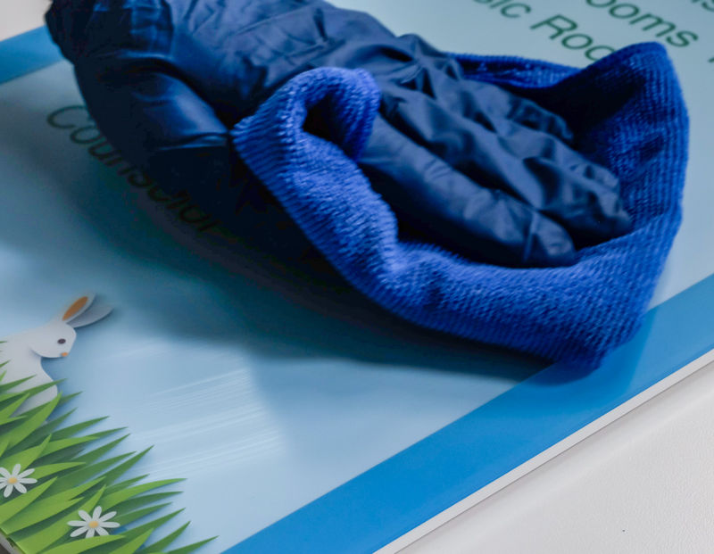 Hand wiping the cleanable acrylic surface of an interior directional sign for a K-6 school.