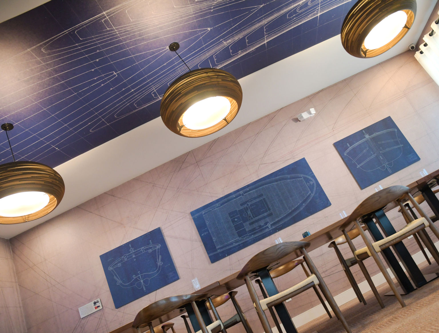Private dinning area surrounded by Amplify wallcovering and Oomph sound absorbing wall panels custom printed with original blueprints form the Penn Yann boat company.