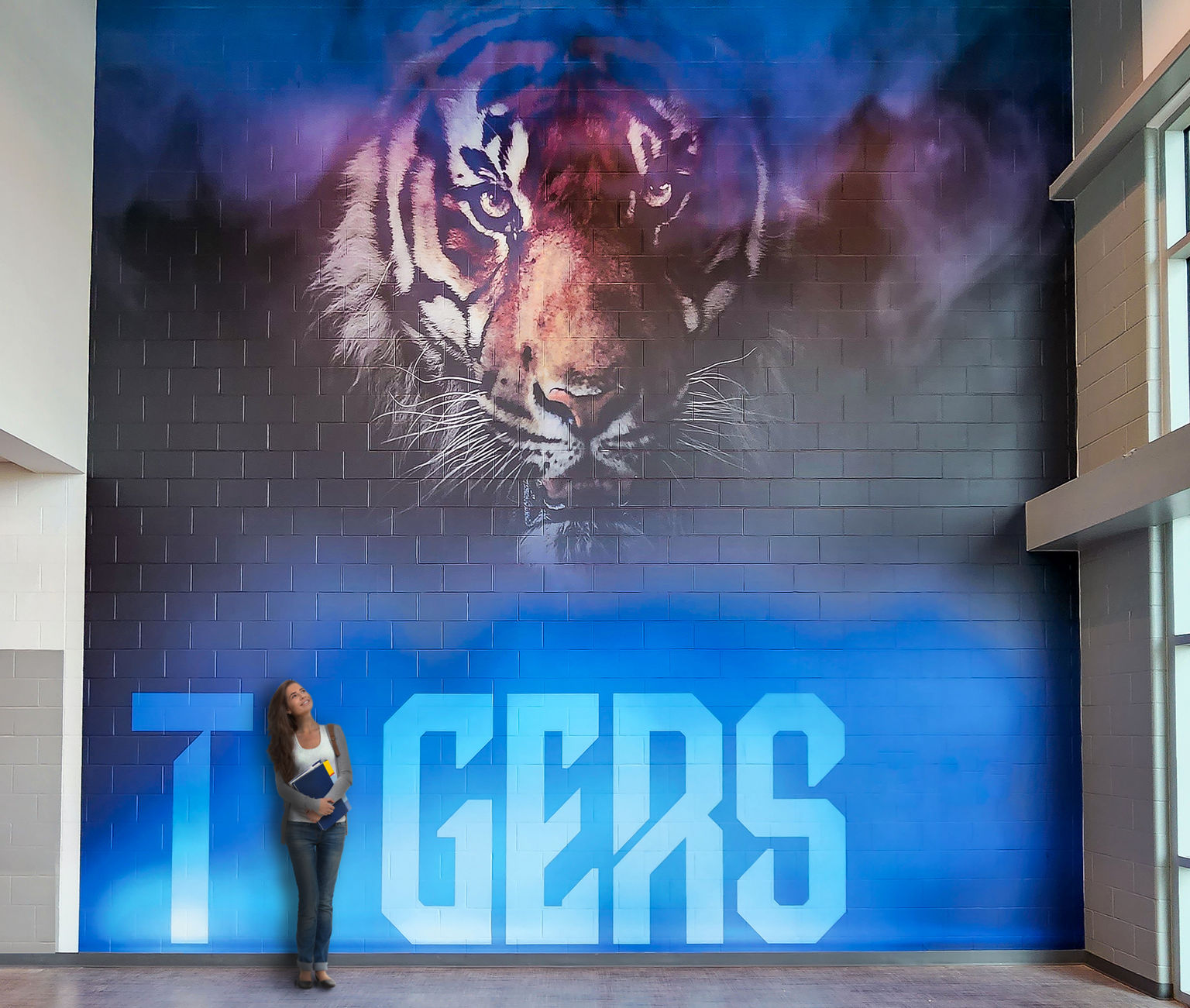 A female student interacting with a multi-story custom past-up wall covering supergraphic on a block wall in a high school featuring a dramatic brand image of a tiger's face.