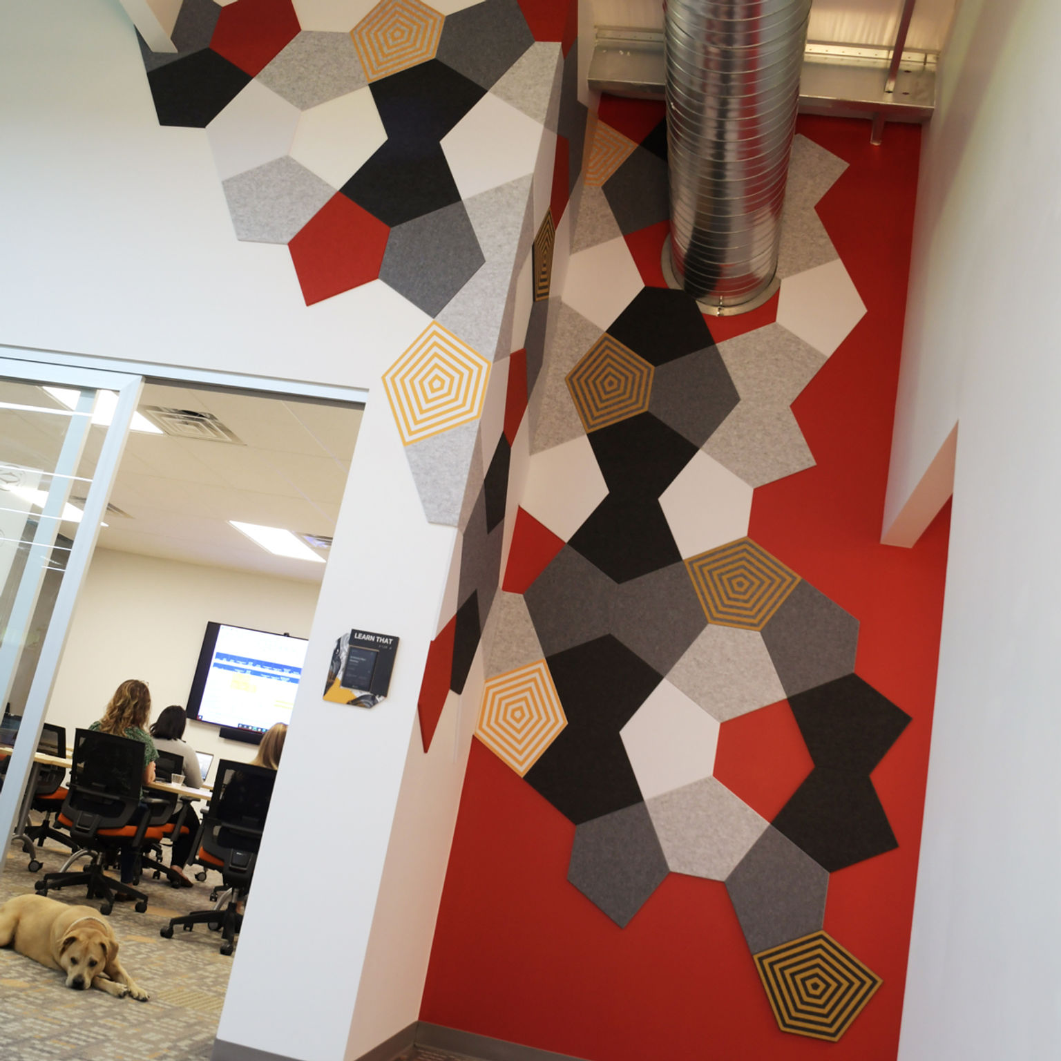 Multi-color custom-printed freeform acoustic tile installation extends across three walls near a design studio