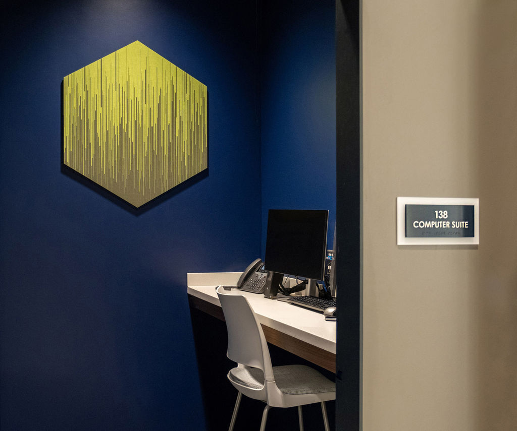 A single green hexagon-shaped acoustic tile with a printed graphic line pattern on a blue wall in a computer suite