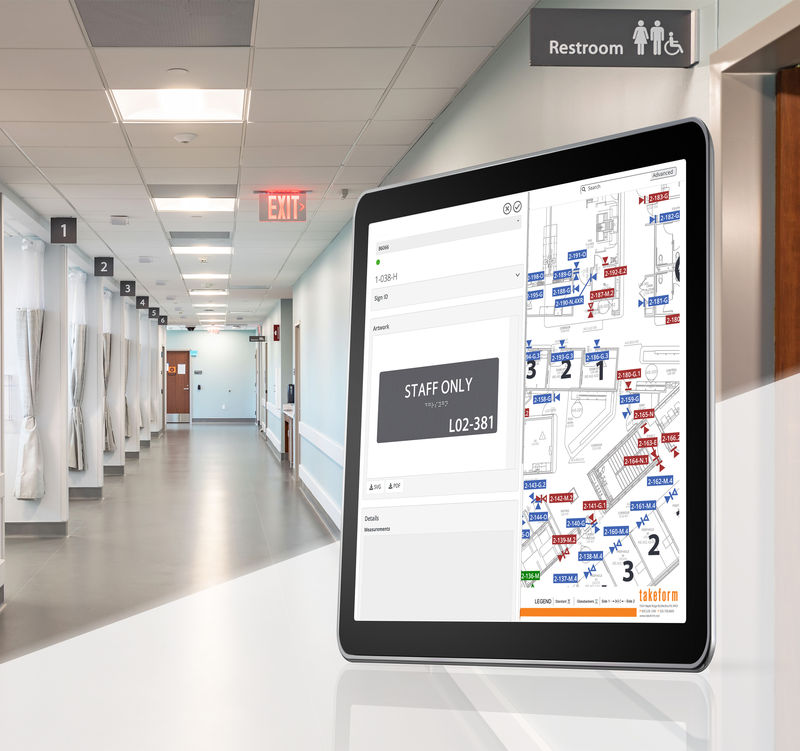 Takeforms sign management platform displayed on a tablet screen with a photo of a hospital hallway and multiple interior signs.