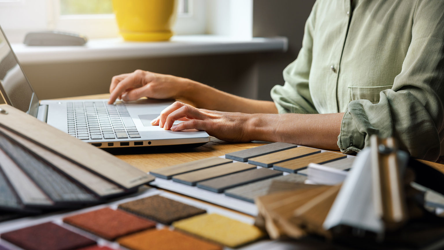 A woman on her laptop with material samples laid out on her desk..