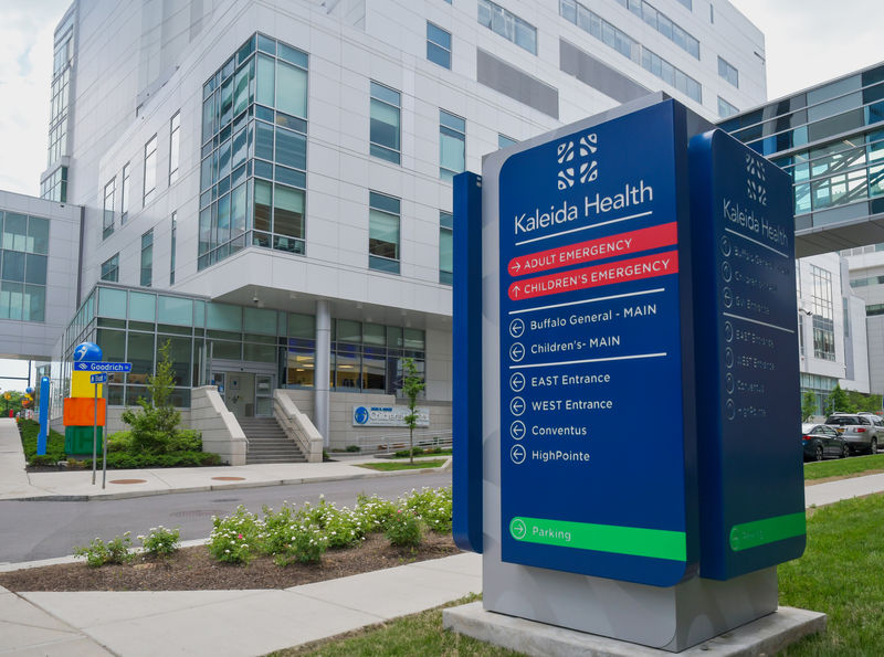 A massive exterior wayfinding monument sign stands in the middle of a busy intersection outside a city Hospital.