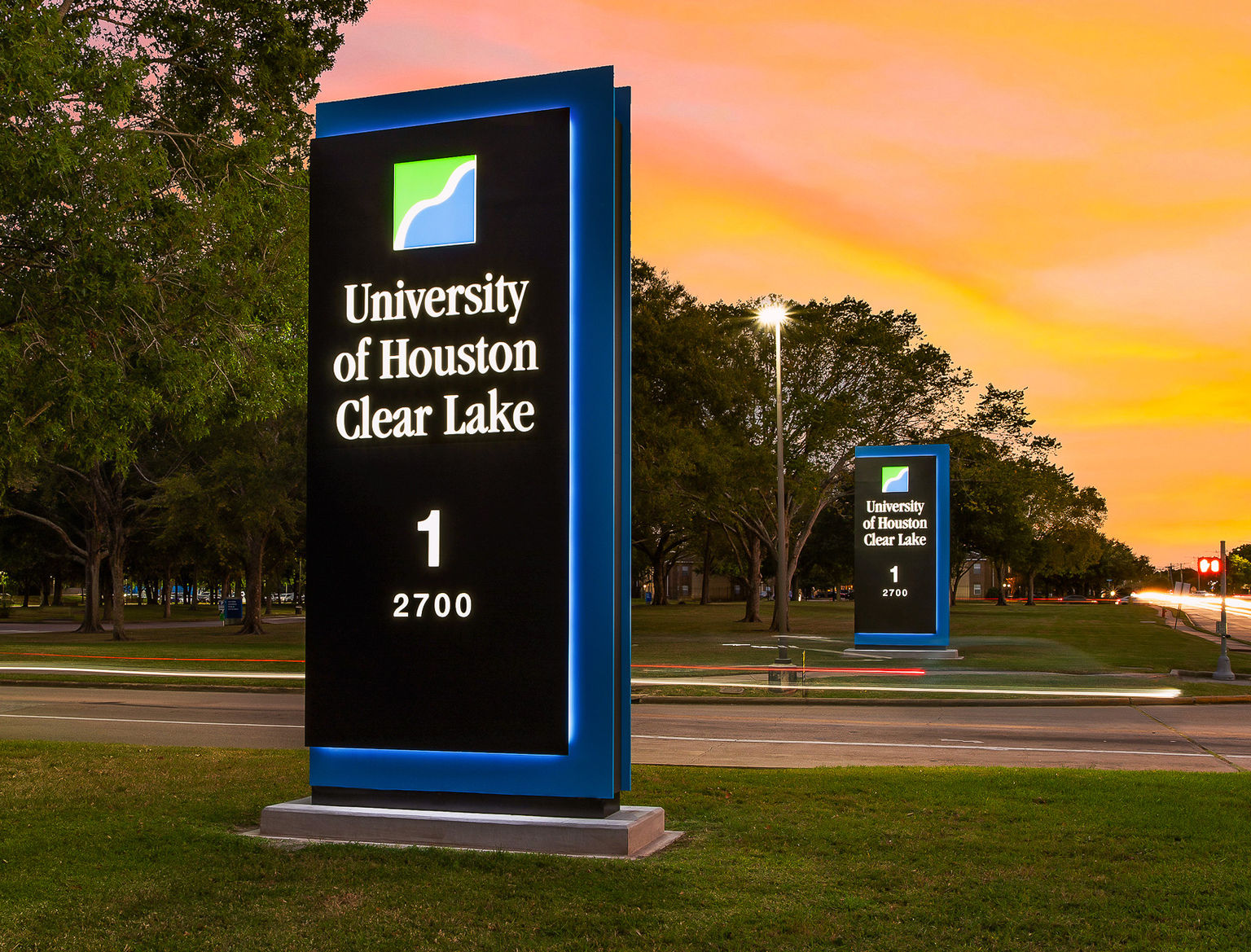A twilight view of two sizeable illuminated branded monument signs at the main entrance of the University of Houston campus.