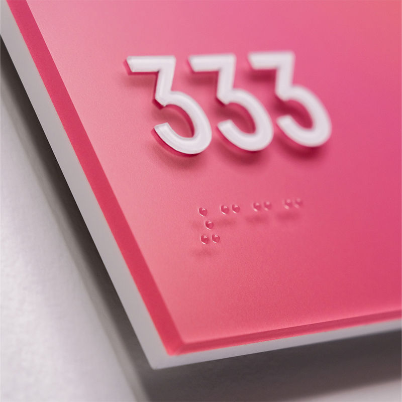 Close-up detail of "333" tactile lettering and Braille on a custom-printed pink ADA room identification sign