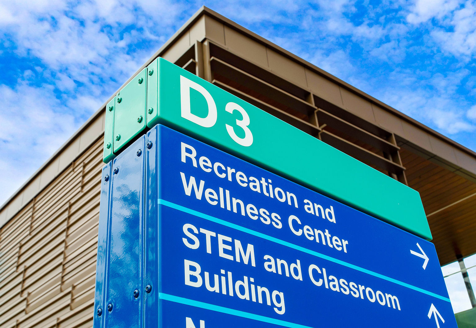 A porcelain coated exterior directional sign complimenting a college building that stands behind it.