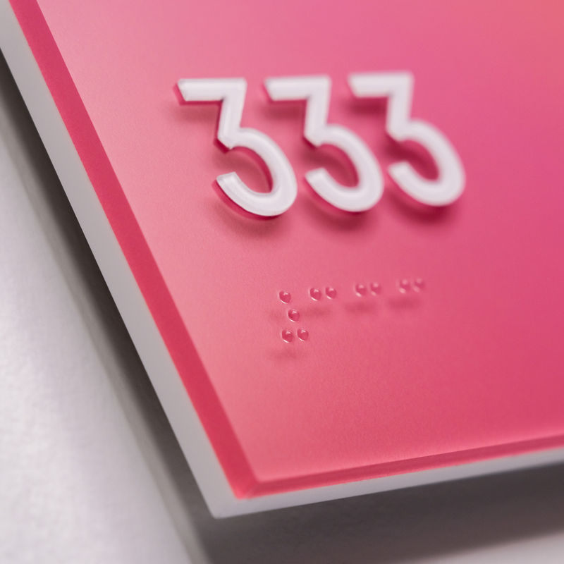 Detail view of an ADA tactile lettering and Braille on a pink room ID sign
