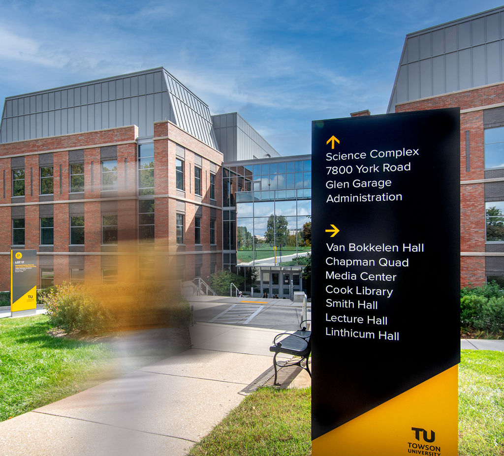 Two large exterior wayfinding signs on a collage campus with a student walking by.