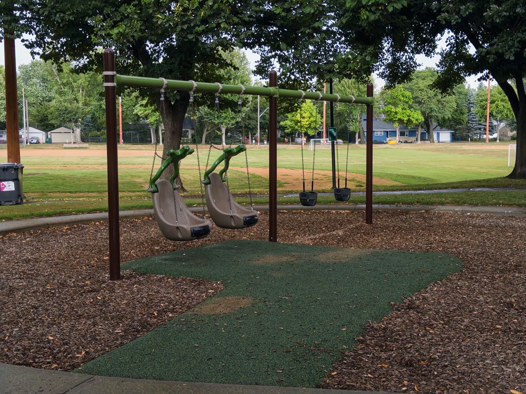 A set of swings at Linden Hills park, featuring two accessible chair swings (with a rubber path) and two infant bucket swings.
