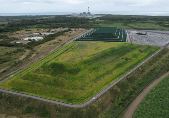 Aerial view of a vegetated, capped landfill mound near the coast