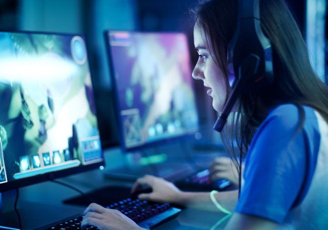 Professional Girl Gamer Plays in MMORPG/ Strategy Video Game on Her Computer. She's Participating in Online Cyber Games Tournament, Plays at Home, or in Internet Cafe. She Wears Gaming Headset.