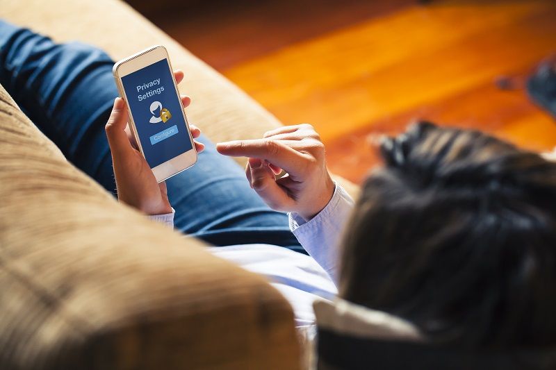 Woman configuring privacy settings on the mobile phone at home. Blue screen. She is laying on the sofa.