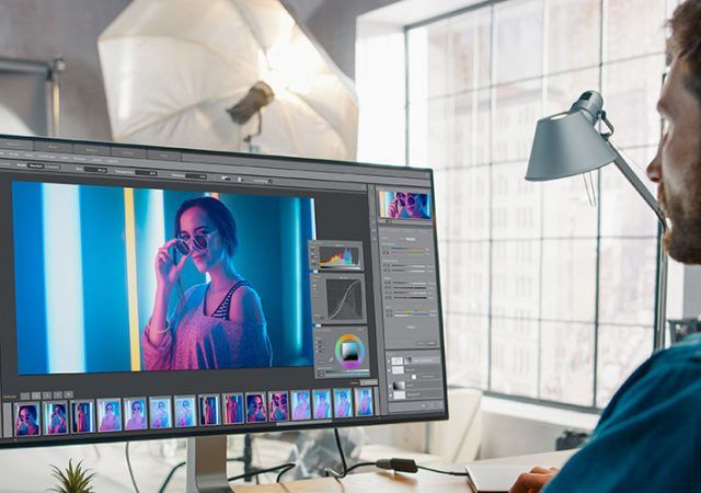 Professional Photographer Sitting at His Desk Uses Desktop Computer in a Photo Studio Retouches. After Photoshoot He Retouches Photographs of Beautiful Female Model in an Image Editing Software