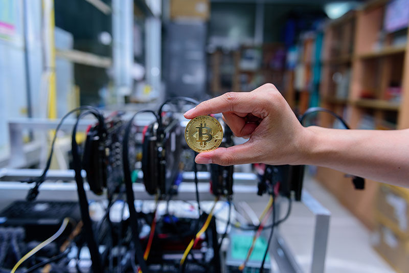 man's hand holding golden Bitcoin on Bitcoin mining background