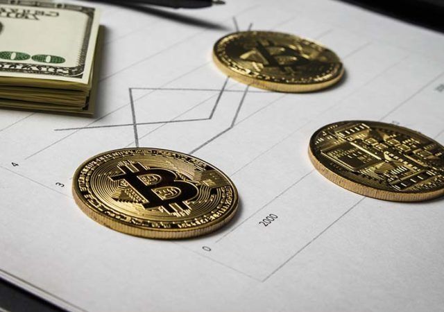 Coins in the form of bitcoin with a bundle of dollars on sheets of statistics