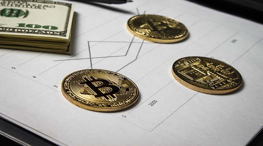 Coins in the form of bitcoin with a bundle of dollars on sheets of statistics
