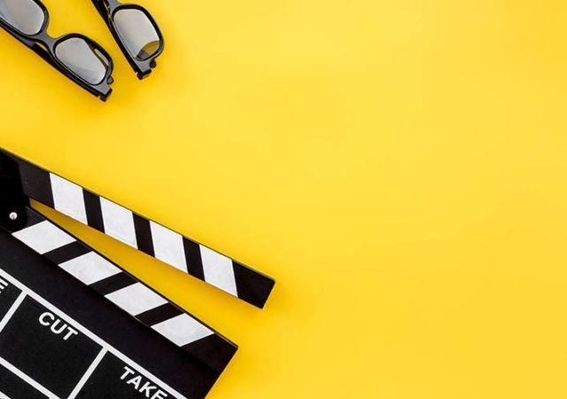 Filmmaker accessories. Clapperboard and glasses on yellow background top view.
