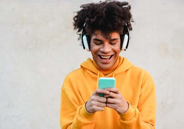 Happy african millennial guy listening music playlist with smartphone app outdoor - Young man having fun with technology trends - Tech, generation z and stylish concept - Focus on face