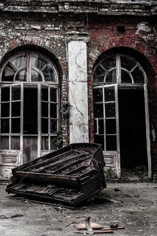 A crumbled grand piano in front of a ruined building.