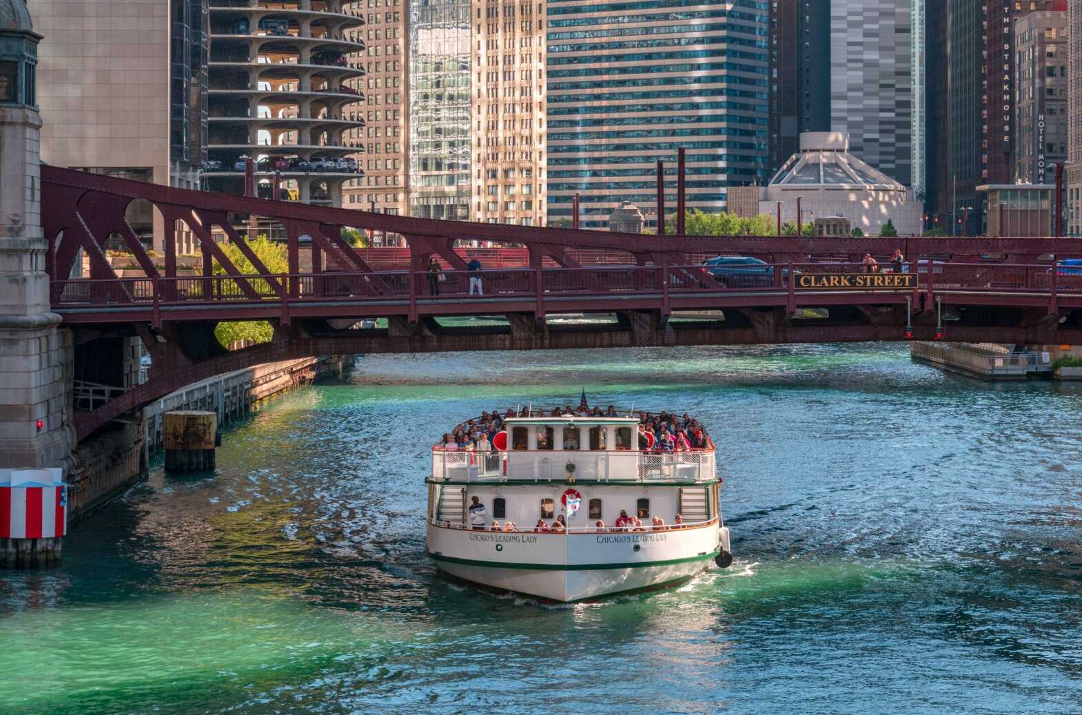 A large passenger boat going down the Chicago river with skyscrapers surrounded the image