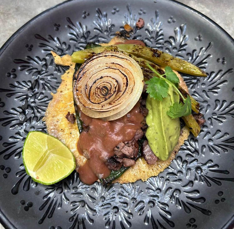 Grilled meat topped with sliced onion and herbs served on a tortilla with lime and roasted vegetables on a decorative gray plate Grilled meat topped with sliced onion and herbs served on a tortilla with lime and roasted vegetables on a decorative gray plate