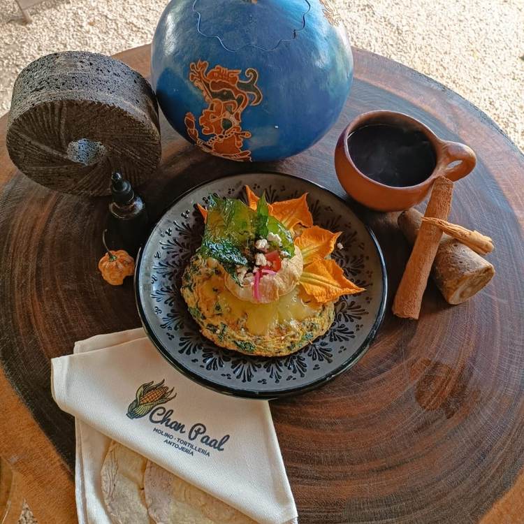 A plated omelet topped with greens and radishes sits on a wooden table alongside a blue decorative bowl, terracotta pitcher, cinnamon sticks, and a napkin with A plated omelet topped with greens and radishes sits on a wooden table alongside a blue decorative bowl, terracotta pitcher, cinnamon sticks, and a napkin with