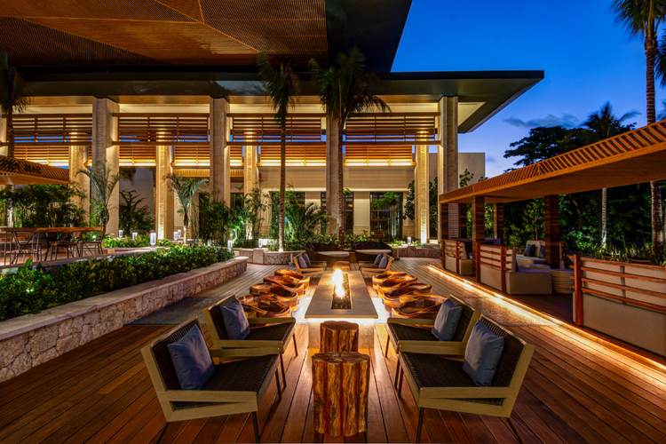 Patio de resort moderno en Tulum luce fogata central rodeada de camastros, con edificios iluminados y vegetación tropical de fondo Patio de resort moderno en Tulum luce fogata central rodeada de camastros, con edificios iluminados y vegetación tropical de fondo