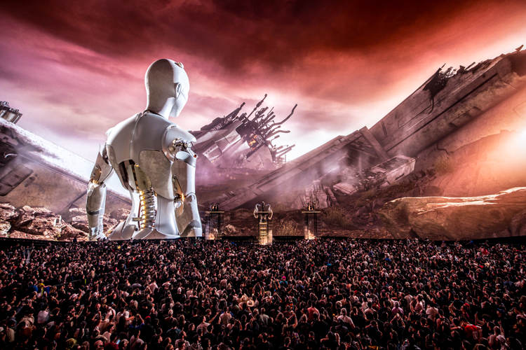 A large mechanical humanoid figure stands before a massive crowd under a dramatic red and purple sky with industrial structures in the background A large mechanical humanoid figure stands before a massive crowd under a dramatic red and purple sky with industrial structures in the background