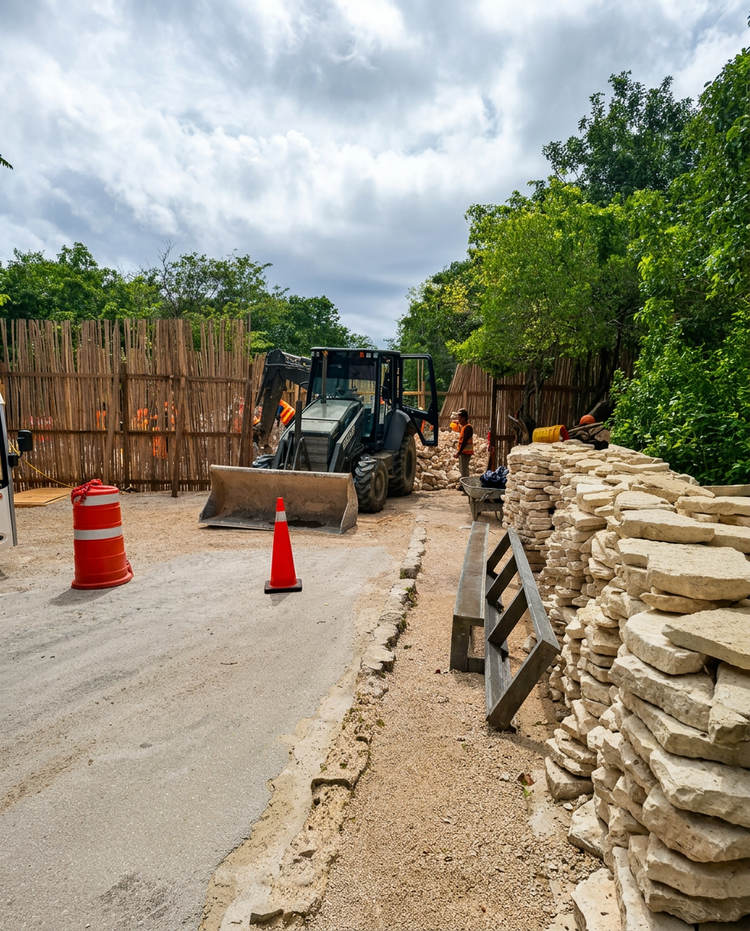 Heavy equipment operators work at a construction site surrounded by stacked stone blocks and wooden barriers in a forested area Heavy equipment operators work at a construction site surrounded by stacked stone blocks and wooden barriers in a forested area