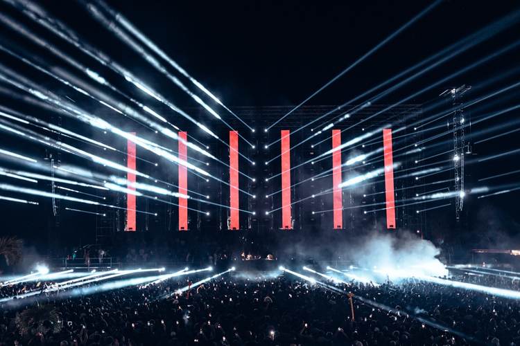 Large crowd gathered in an arena at night under dramatic red vertical banners and blue stage lighting Large crowd gathered in an arena at night under dramatic red vertical banners and blue stage lighting